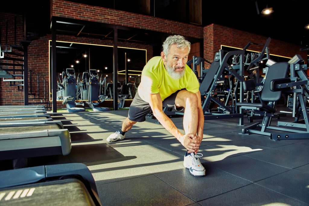 Warming up. Portrait of athletic middle aged man in sportswear stretching legs before training in