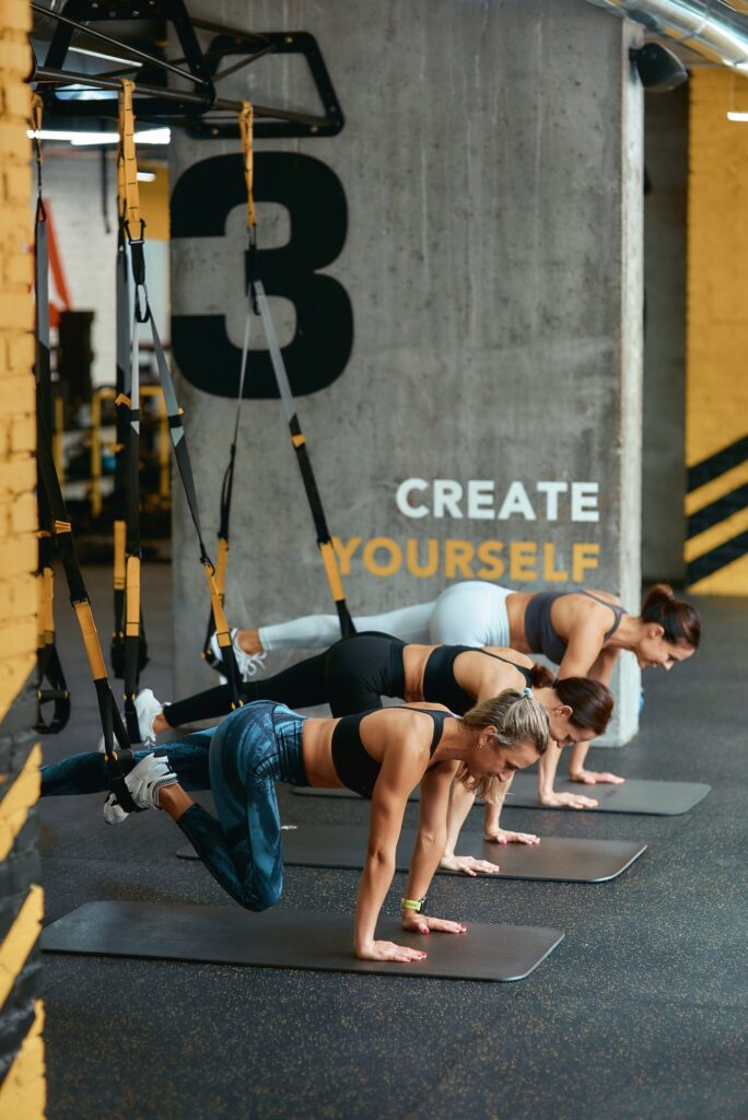 Suspension training. Three young athletic women exercising with trx fitness straps at gym, vertical